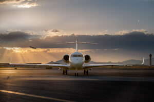 Head-on view of a private jet on the tarmac at sunset, with dramatic light rays, a departing commercial jet by Aircraft Photographer in Nashville