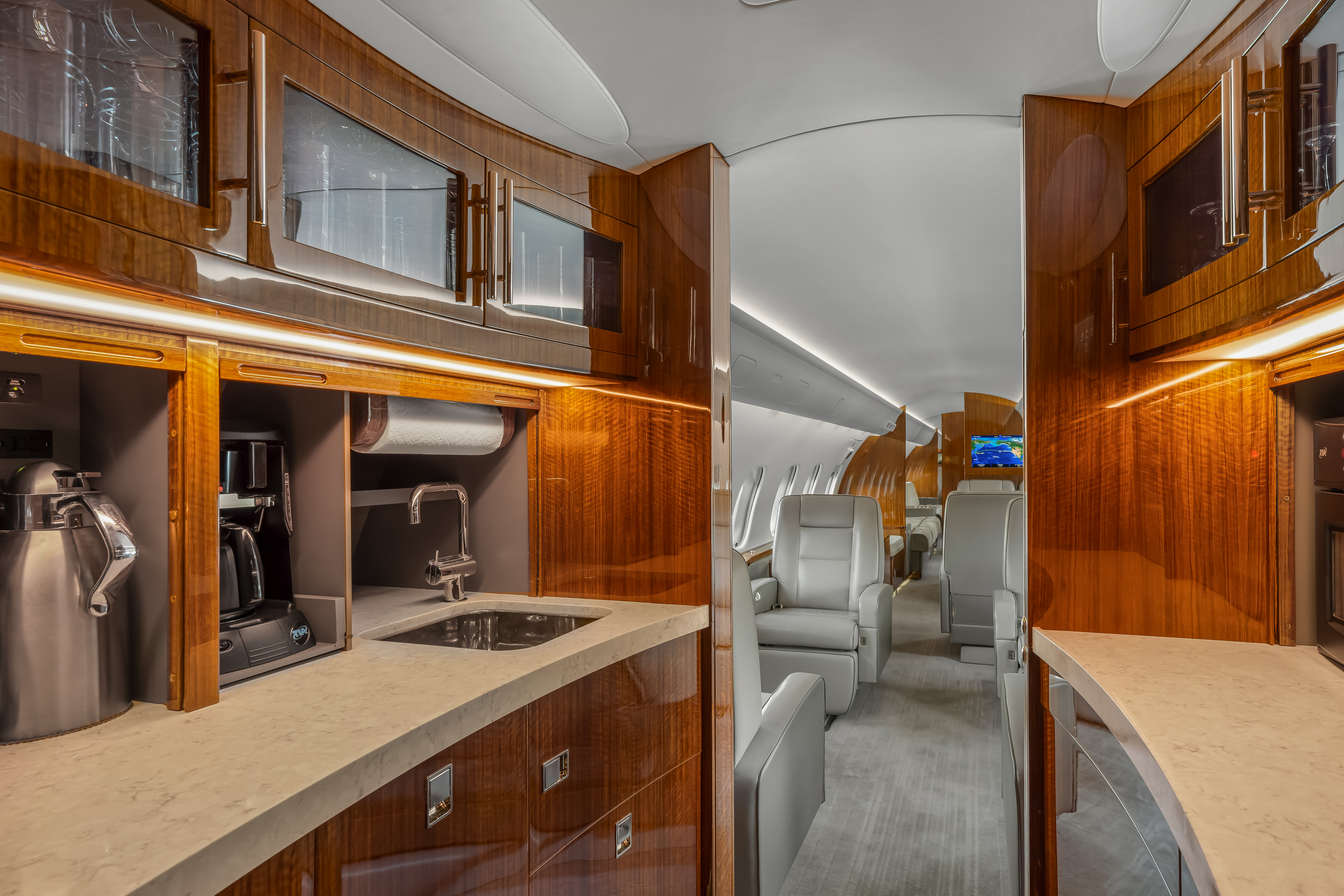 Luxury private jet galley in Palm Springs with glossy wood cabinetry, glassware storage, and a view into the main cabin seating area