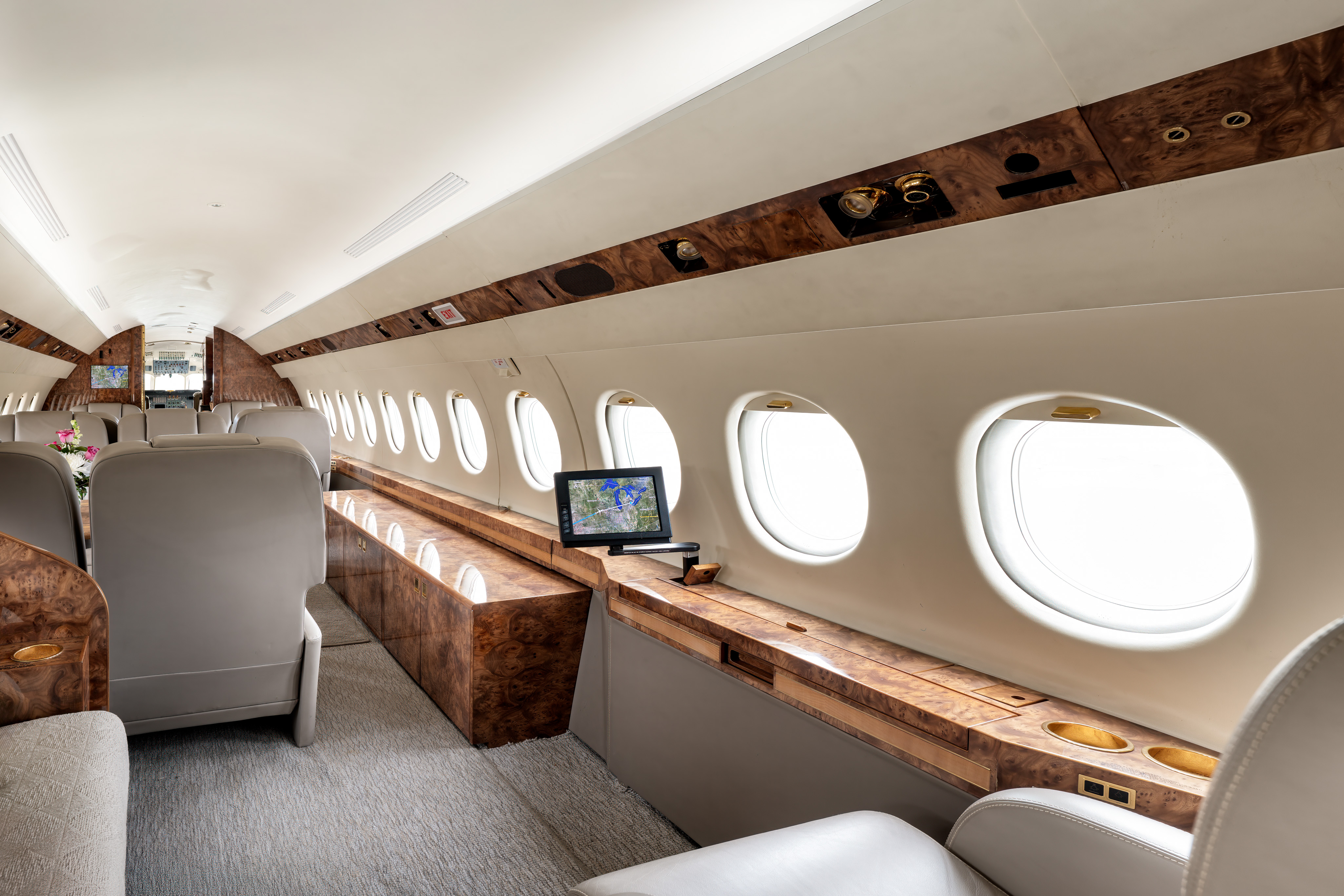 Spacious private jet cabin in Palm Springs featuring multiple oval windows, cream leather seating, and polished wood accents with a cabin map display