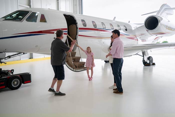 Aircraft photography production scene with a family boarding a private jet in a Dallas Addison Airport hangar, guided by ground crew.