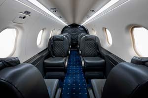 Business jet cabin with black diamond-stitched leather seats and blue carpet photographed by AeroMedia on the ramp at Nîmes–Alès–Camargue–Cévennes Airport, France