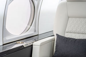 Luxury private jet cabin detail in the Caribbean showing a white quilted leather seat, adjustable armrest controls, and large cabin window.