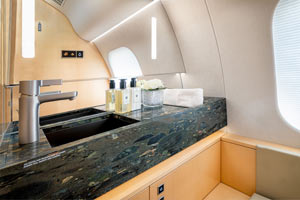 High-end private jet lavatory in the Caribbean with stone countertop, premium fixtures, and light wood cabinetry.