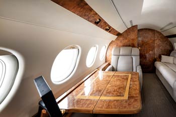Falcon 900 private jet interior with high-gloss burl wood cabinetry and premium leather seating photographed at San Jose International Airport