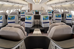 Spacious business class airplane cabin with reclining seats and personal entertainment screens