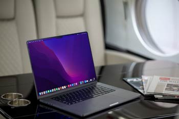 Private jet cabin detail in Cairns showing an open laptop on a glossy wood table with newspapers and soft leather seating