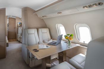 Private jet cabin table with laptop and polished wood surface, photographed at Macau International Airport.