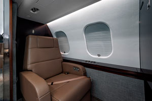 Private jet cabin seat in the Caribbean featuring tan leather upholstery, modern cabin paneling, and closed window shades