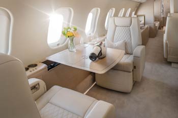 Luxury private jet cabin in soft beige tones with wine service, fresh flowers, and reclining leather seats during a Naples, Florida aircraft photoshoot. Aircraft Photographer in Naples