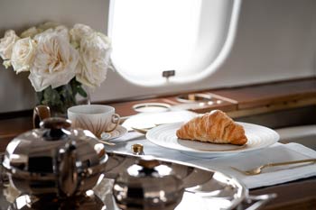 Elegant private jet table display featuring silver tea service, croissant, and white rose arrangement with bright cabin window light at Miami’s Opa Locka Airport.