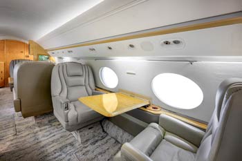 Aircraft Photographer in Los Angeles Private jet forward cabin with gray leather club seating, extended wood table, and large round windows, photographed at Ontario International Airport.