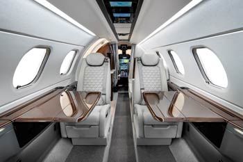 Private jet interior with premium leather seating and polished wood tables facing the cockpit, photographed at Naples Airport in Florida.