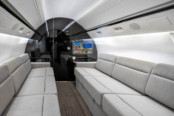 Spacious private jet lounge cabin with dual gray sofas, glossy rear bulkhead, and moving map display, photographed at Istanbul Airport.