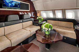 Elegant private jet lounge featuring beige leather sofas, wood tables, and fresh flower arrangements.