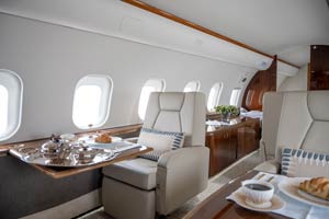 Luxury inflight dining setup with a croissant, fine china, silver tea service, and white roses inside a private jet at Opa Locka Executive Airport in Miami