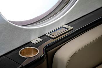 Private jet cabin window and side console showing touch panel, USB port, and cupholder, photographed at Macau International Airport.