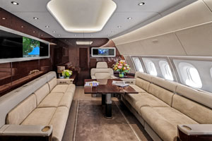 Luxury private jet interior with large sofas, conference table, and wall-mounted monitors