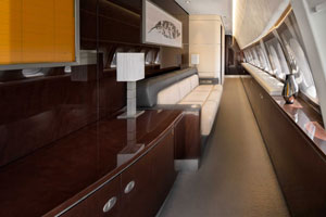 Exclusive private jet cabin featuring glossy wood paneling, a beige sofa, and modern lighting
