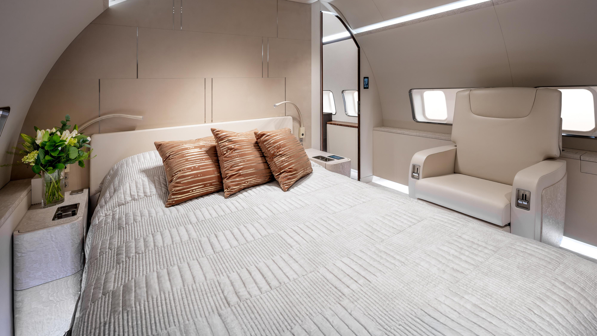 737 MAX private jet bedroom suite in Dallas featuring a full bed with copper accents, side seating, floral arrangement, and warm ambient lighting in a VVIP aircraft interior.