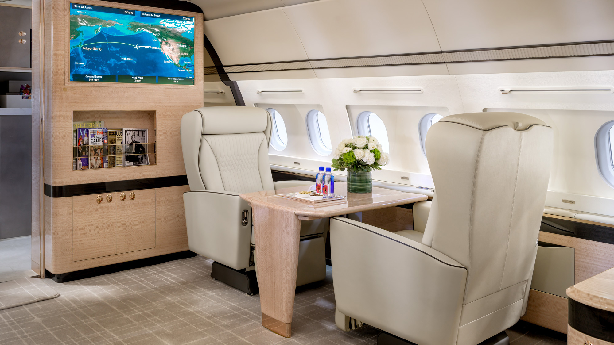 Boeing 737 private jet interior captured in Las Vegas showing a mid-cabin lounge with club chairs, a wall-mounted inflight display, gloss wood paneling, and magazine storage.