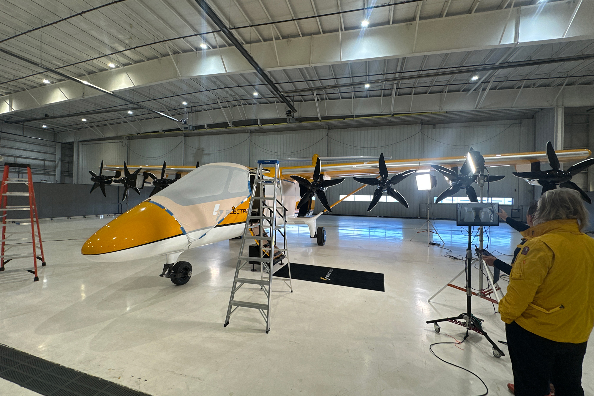 Professional aircraft photography production services in action for the Electra hybrid-electric eSTOL demonstrator inside a Virginia hangar, with crew, lighting rigs, and staging equipment surrounding the prototype aircraft."