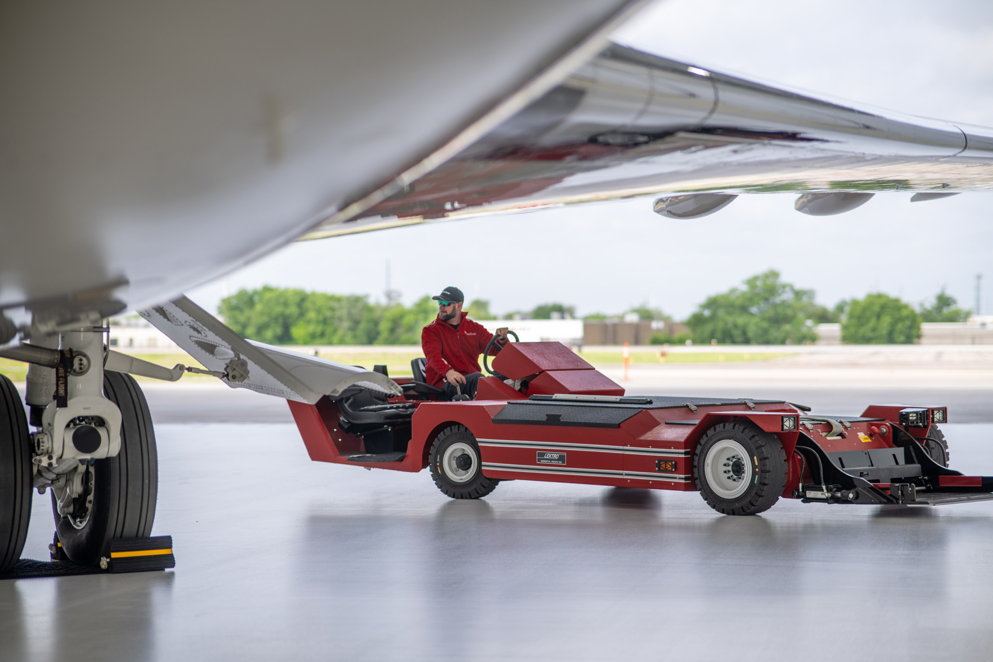Ground-level shot beneath a jet showing a tug operator pulling the aircraft with a red Lektro tug in Austin.
