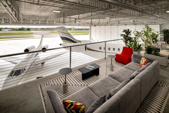 Mezzanine lounge inside Sky Harbour FBO at Addison Airport overlooking a private jet inside the hangar, with modern seating and architectural lighting