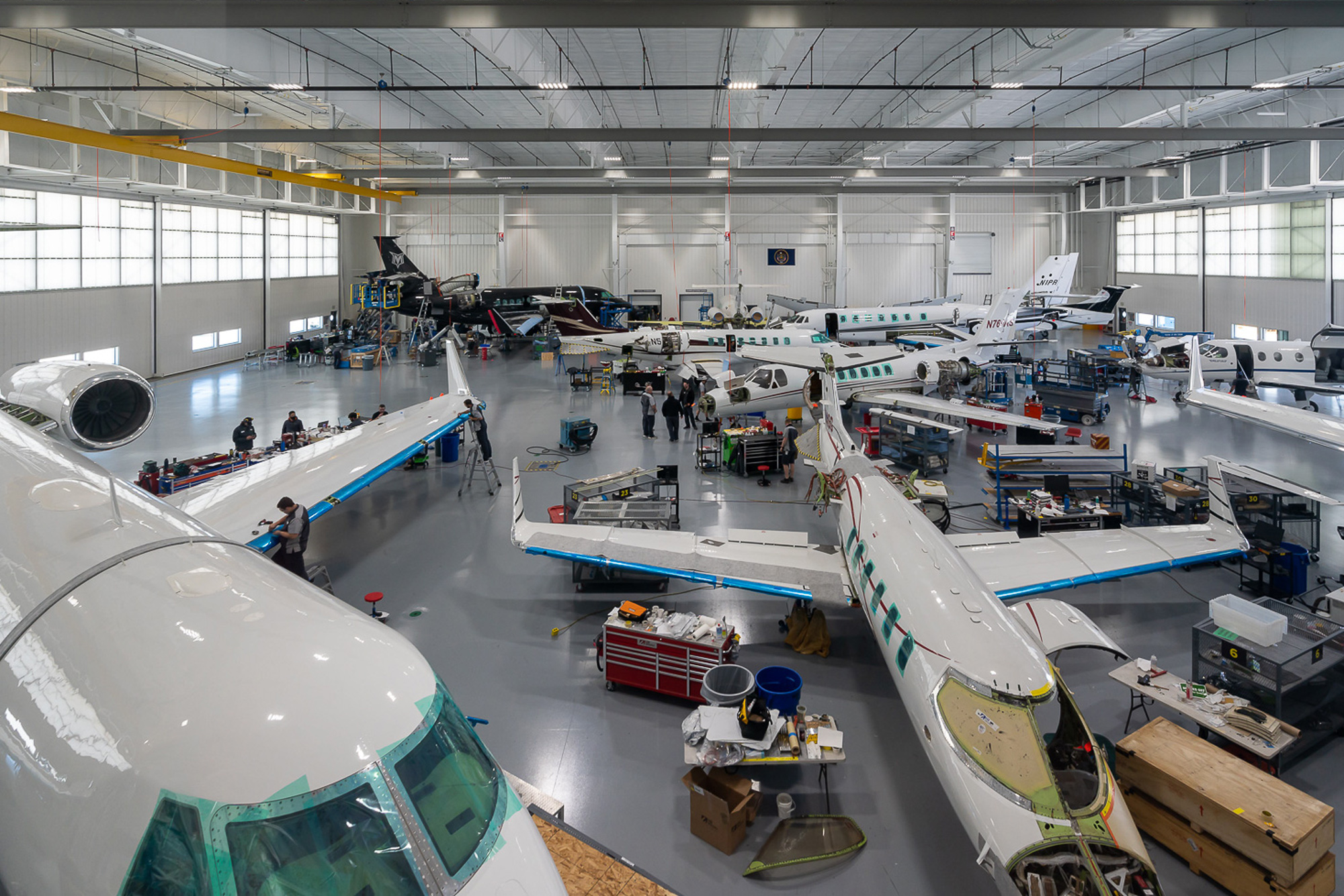 Busy aircraft maintenance hangar in Wichita with multiple private jets and technicians performing inspections, repairs, and modifications.