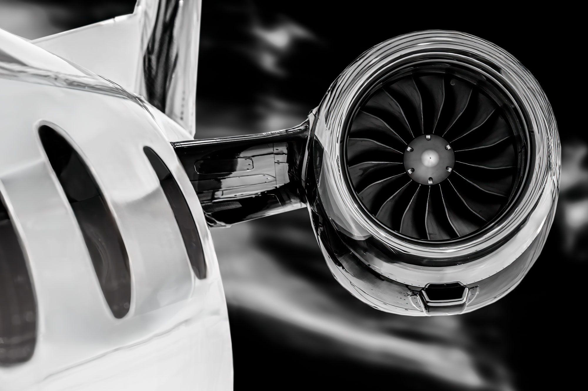 Dramatic close-up of a business jet engine and window reflections in black and white, showcasing the turbine blades and reflective metal surfaces.