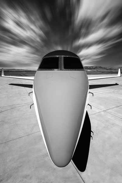 This visually striking black and white artwork captures the aerodynamic nose of a sleek private jet, centered beneath a vortex of motion-blurred clouds that seem to echo the jet's latent speed.